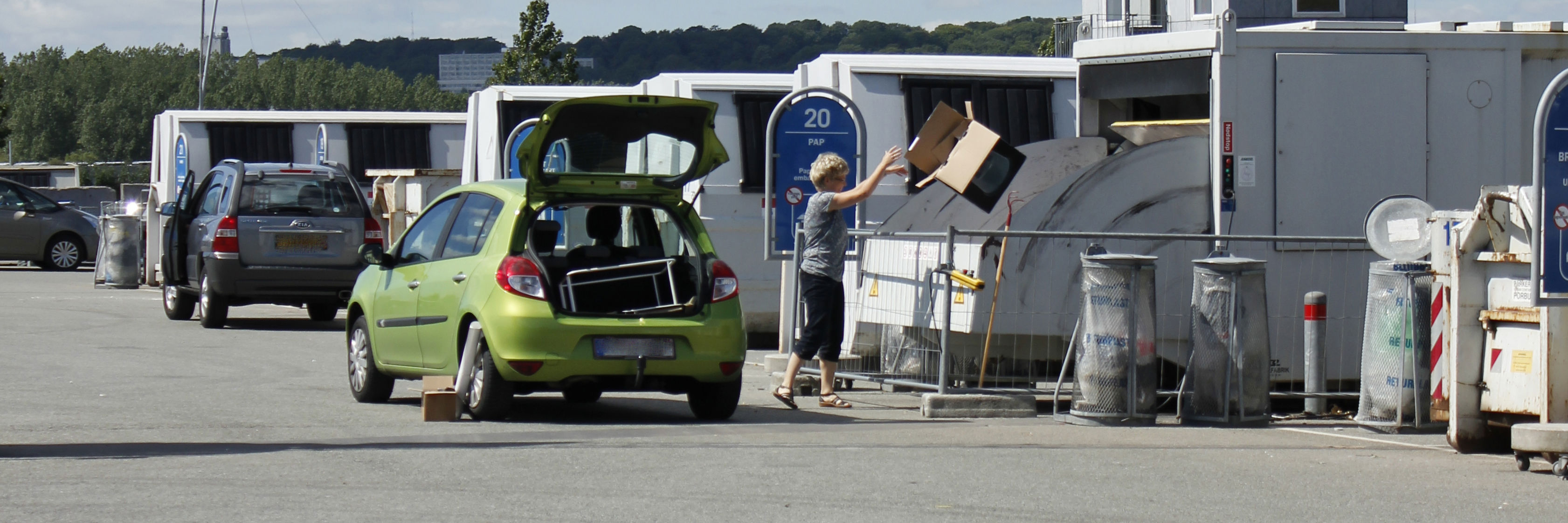 Kvinde smider papkasse i container på genbrugspladsen